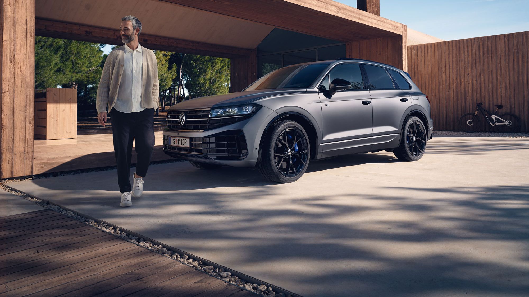 VW Touareg R eHybrid je zaparkovaný pred domom, muž sa od vozidla vzďaľuje