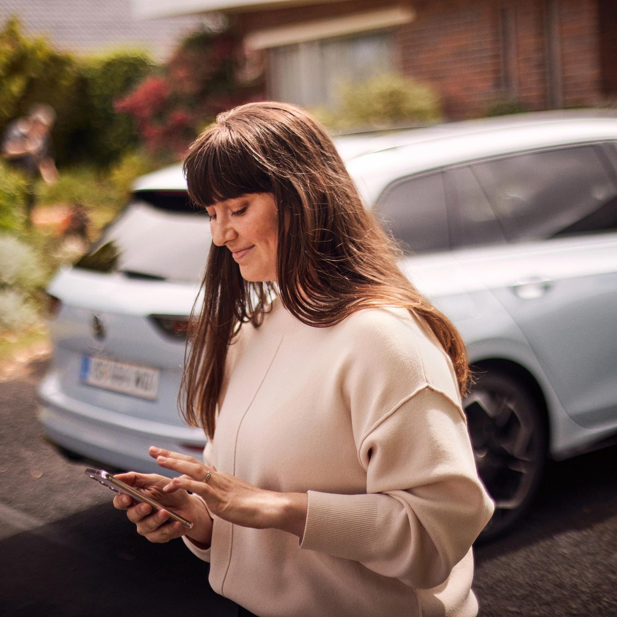 Žena stojí za vozidlom Volkswagen a pozerá na svoj smartfón.