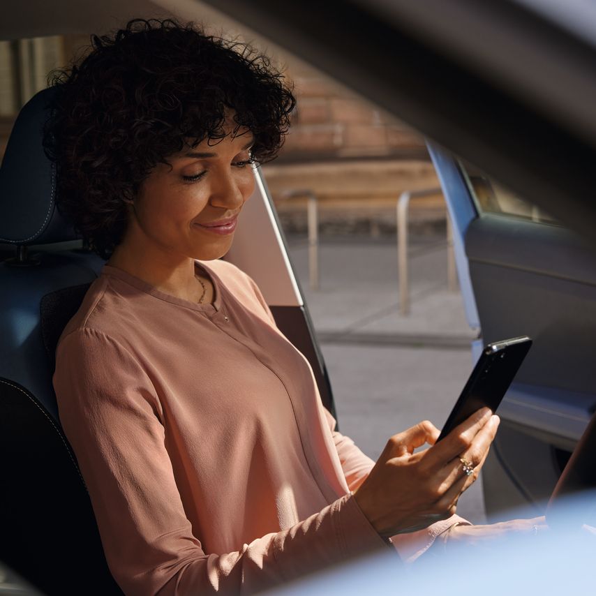 Usmievajúca sa žena na sedadle vodiča zaparkovaného VW T-Cross pozerá na svoj mobilný telefón.