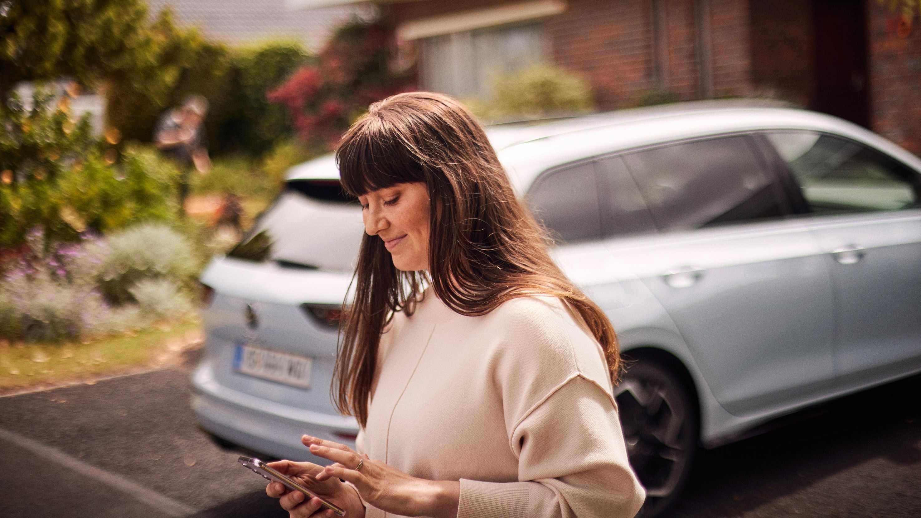 Žena stojí za vozidlom Volkswagen a pozerá na svoj smartfón.