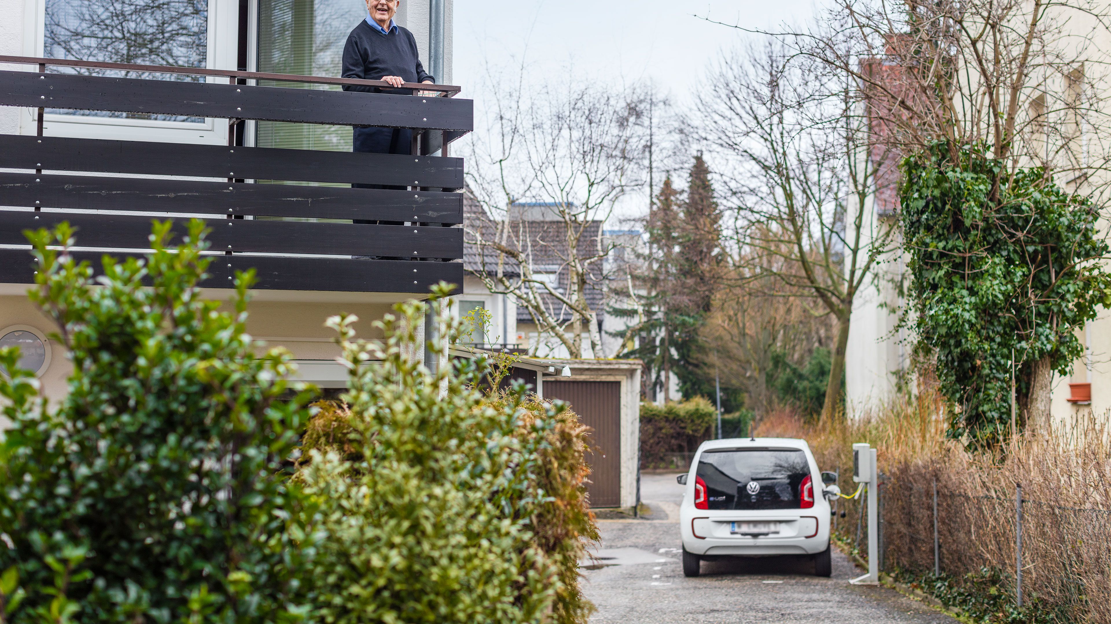 Gerhard Heinz steht auf seinem Balkon und beobachtet seinen e-up! im Hof beim Laden an der Wallbox