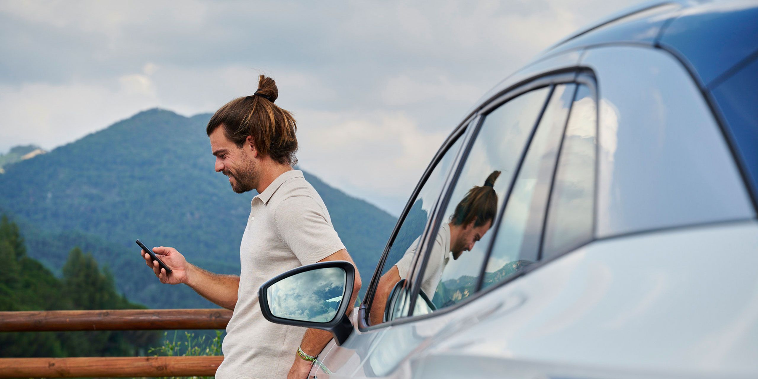 Ein Mann lehnt an einem Volkswagen ID. und blickt auf sein Smartphone.