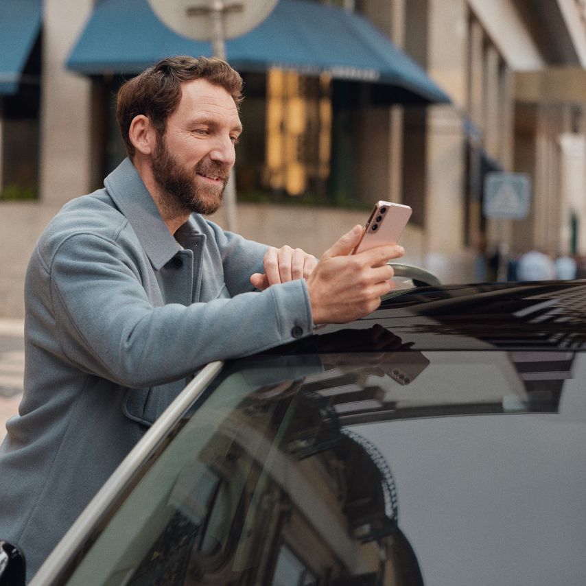 Muž opretý o Volkswagen a pozerajúci sa na svoj mobilný telefón